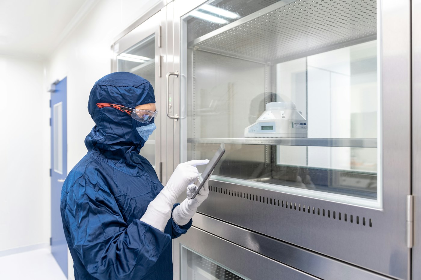 Operator in cleanroom garments checking equipment with a tablet